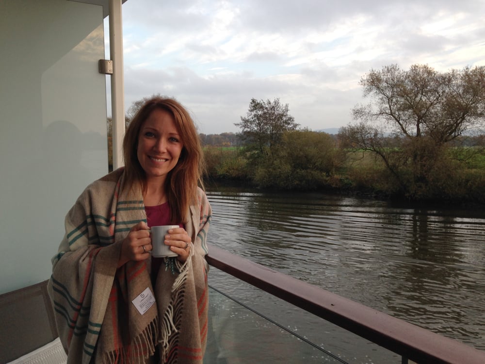 Rachelle wrapped in a blanket holding a coffee while on a Veranda balcony on a Rhine cruise.