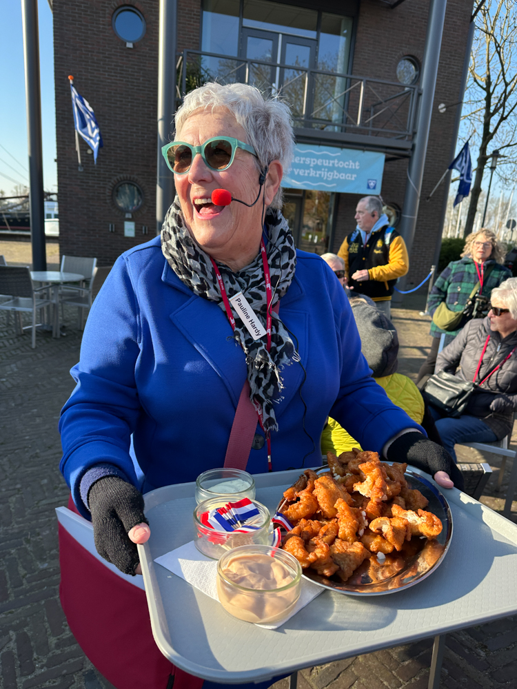 Viking guide in Enkhuizen, wearing a blue jacket and a big smile, offering fried pollock to tour members on the Tulips and Windmills Viking cruise.