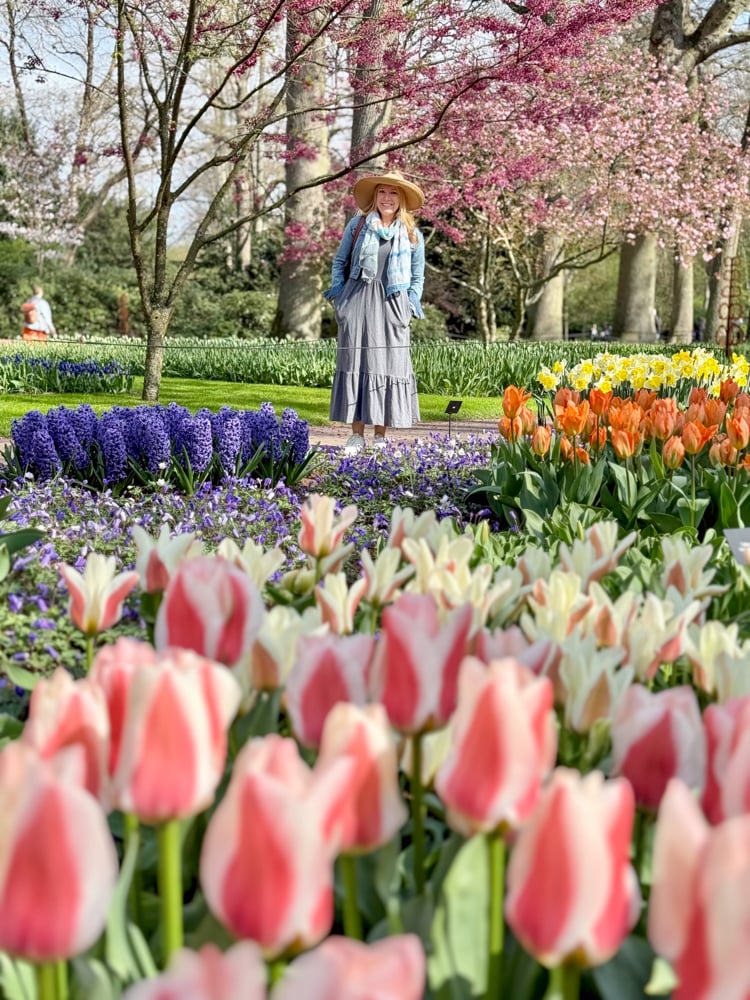 Rachelle sanding under cherry blossom trees by dozens of flowers during a Keukenhof Gardens River Cruise Excursion