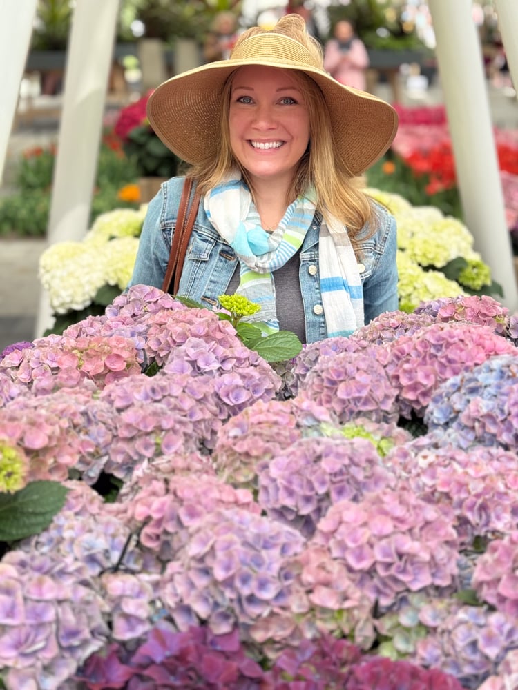 Rachelle standing behind purple hydrangeas