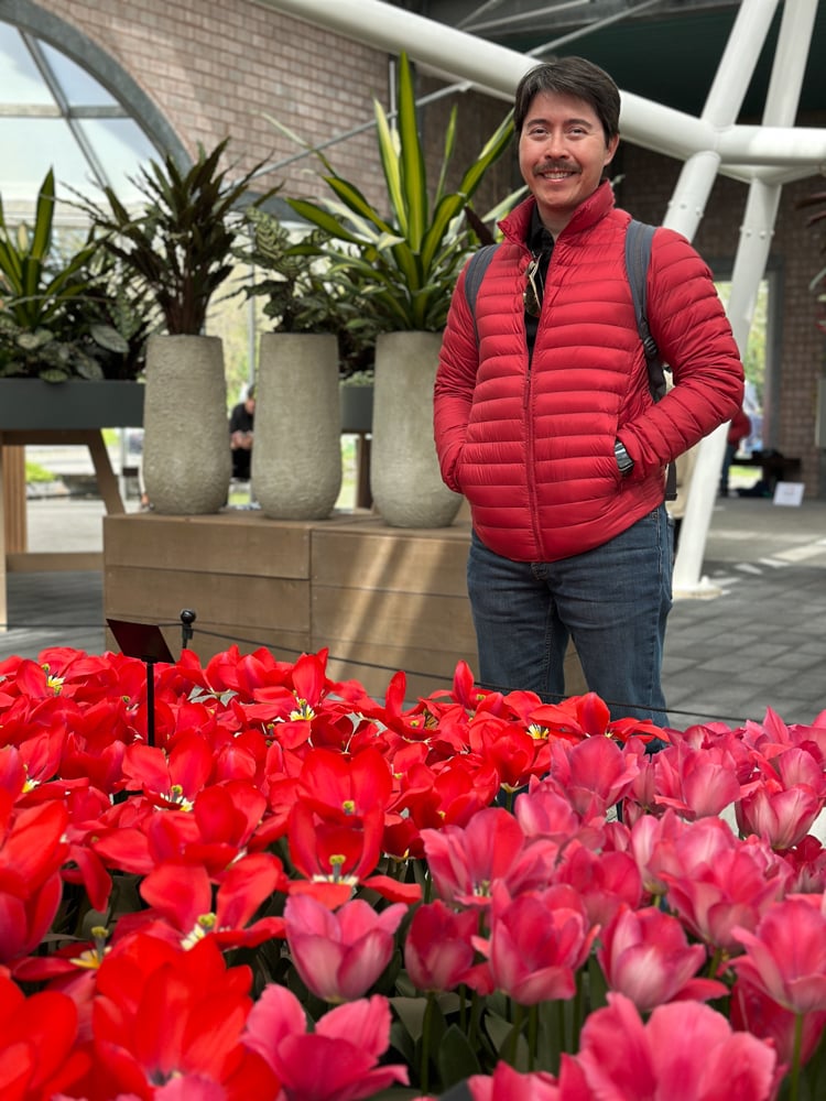 Pete standing by red tulips that match his red jacket